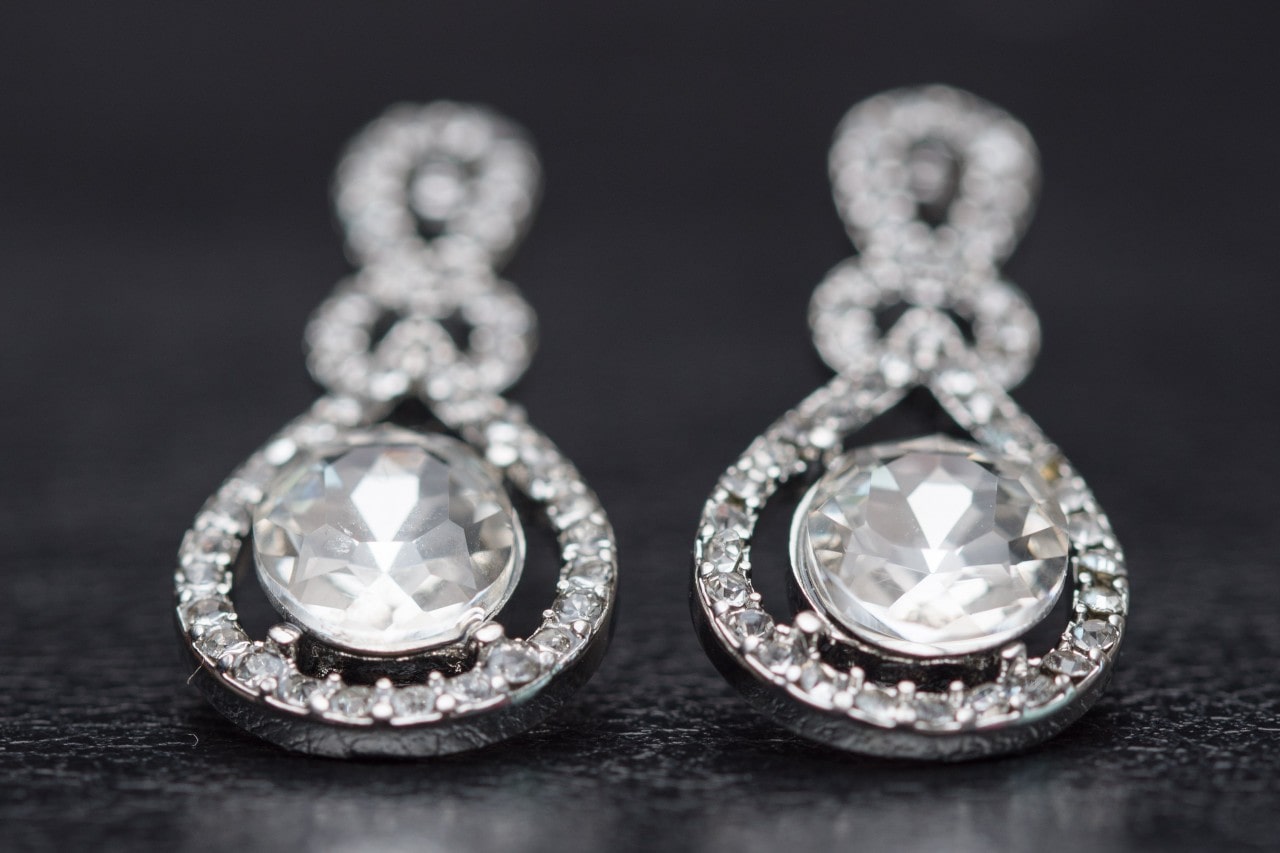 A sparkling pair of diamond earrings from Sylvie sit on a black background