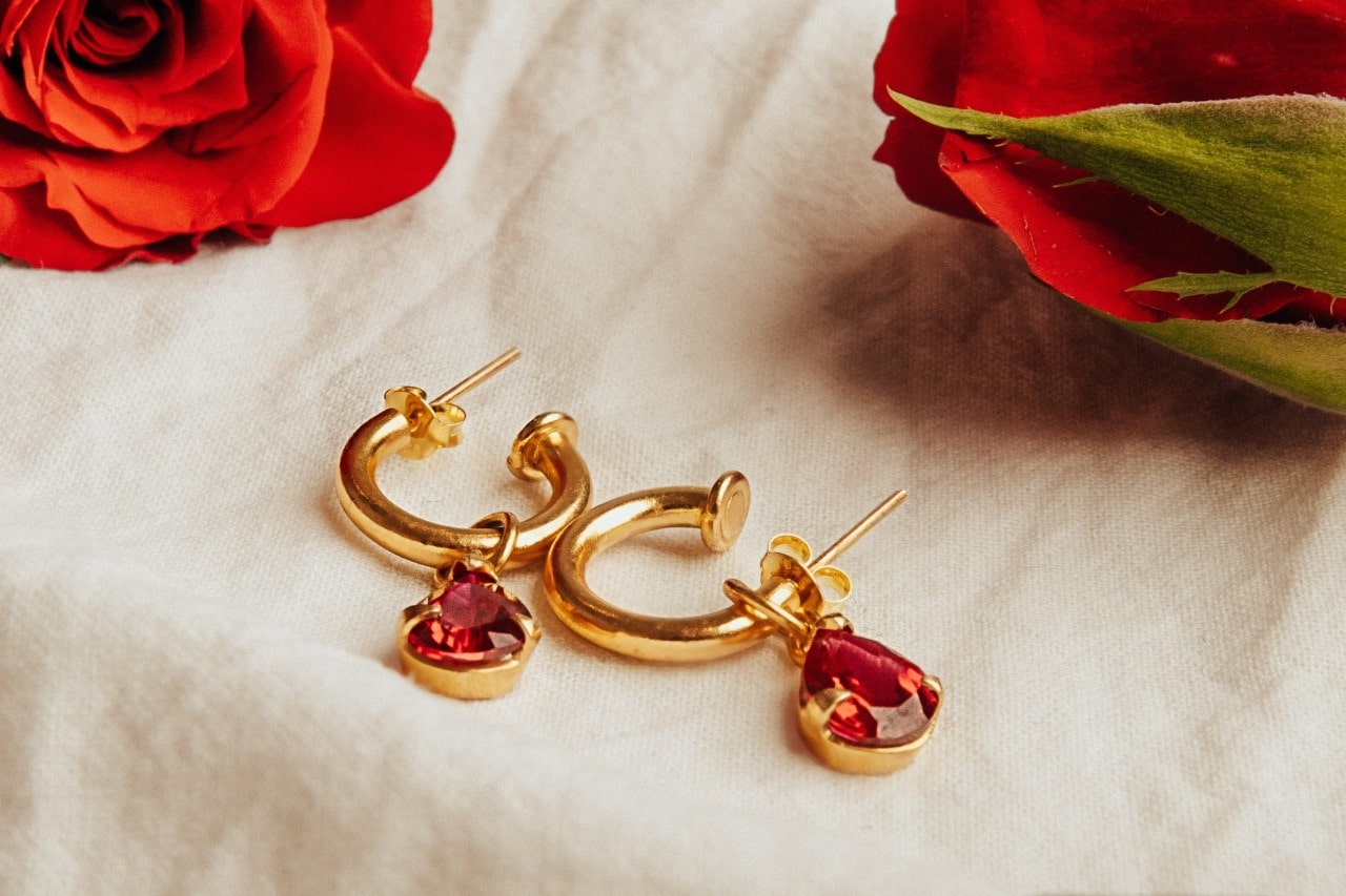 a pair of yellow gold ruby drop earrings next to red roses on a piece of fabric