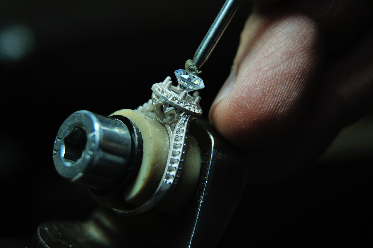 A close-up of a jeweler placing a diamond into a white gold halo engagement ring.