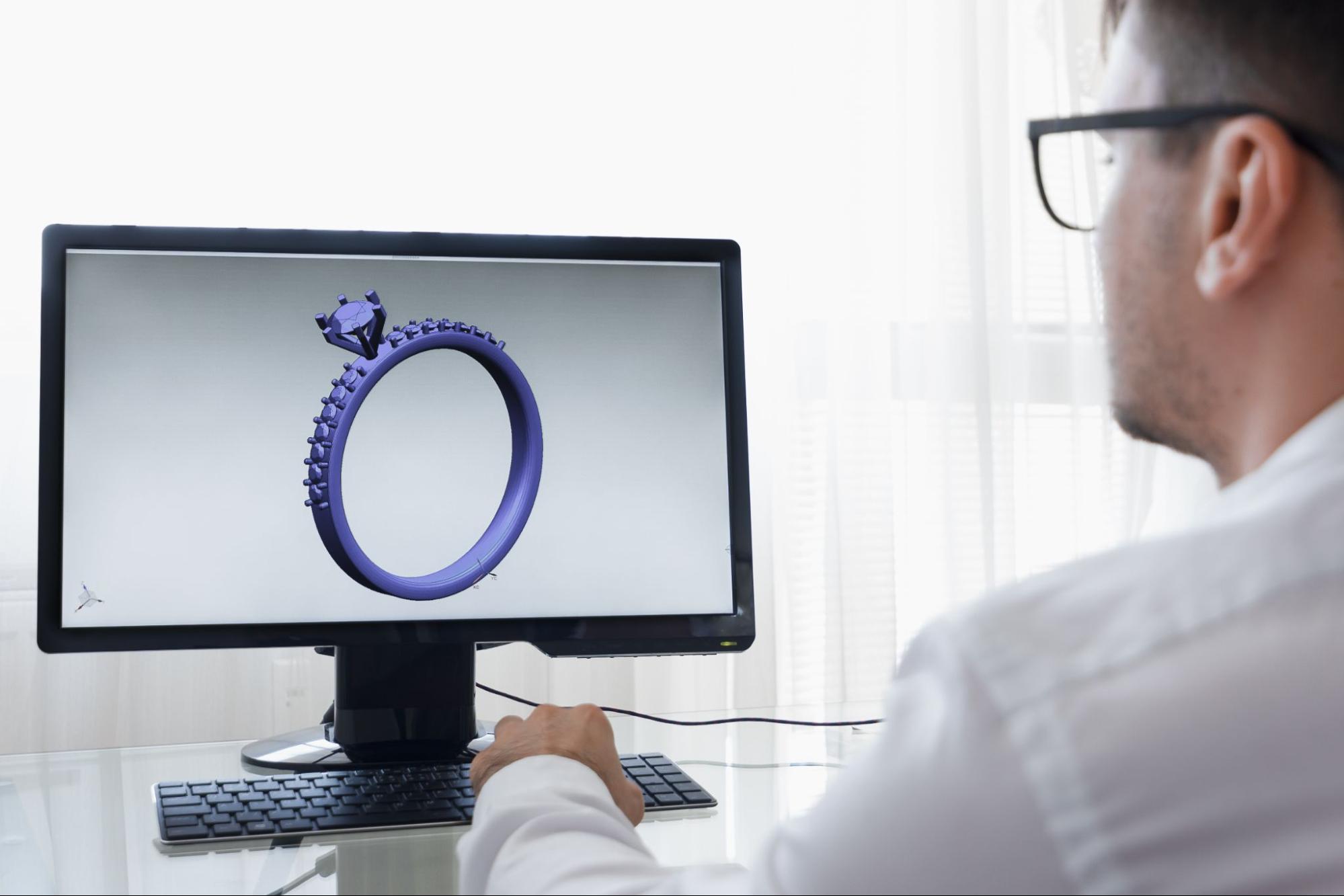 A jeweler sitting in front of a computer with a 3D animation of an engagement ring.