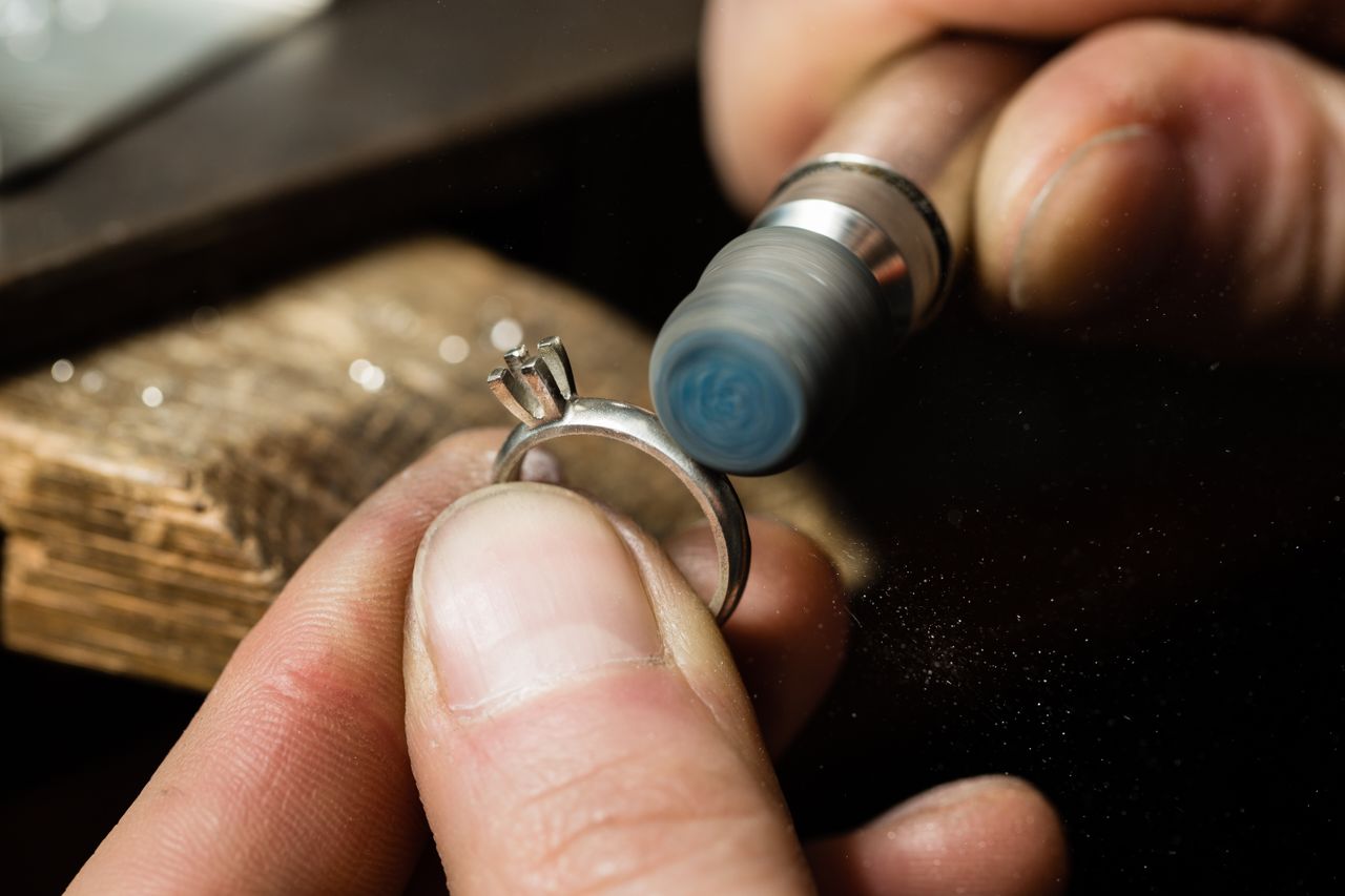 A jeweler polishing a solitaire white gold engagement ring with a special tool.