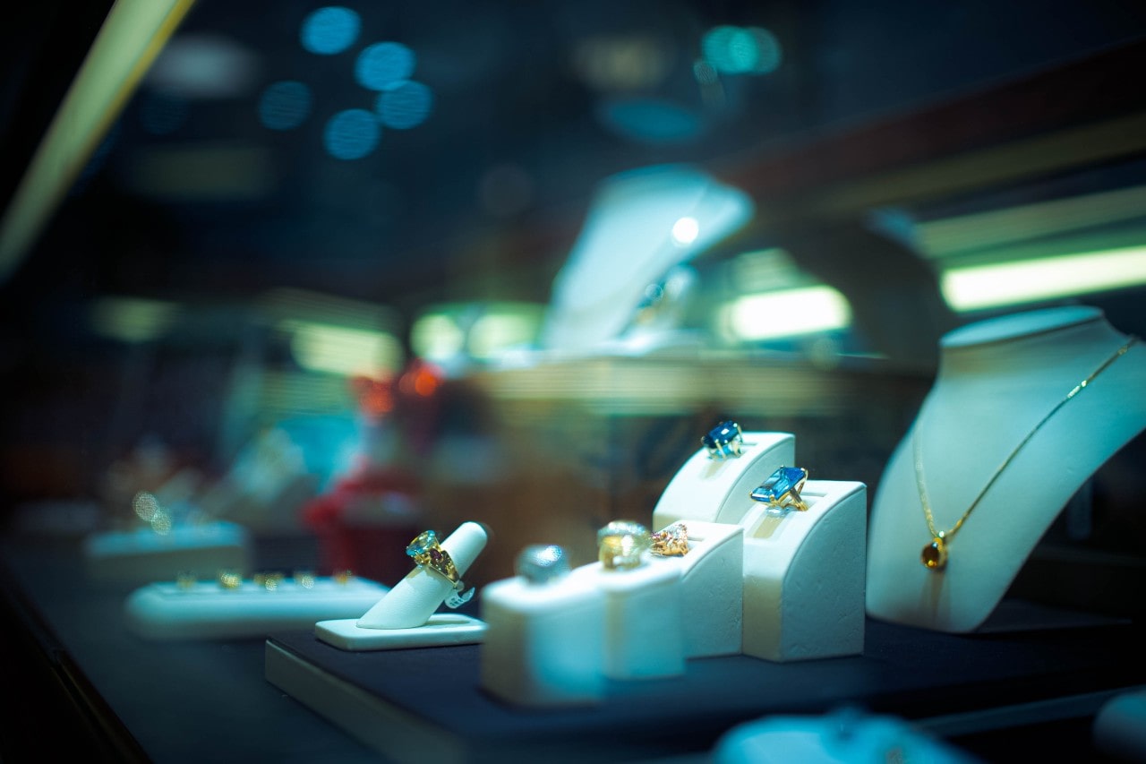 Close-up of a jewelry store display featuring rings with gemstones and a gold necklace against a soft-focus background.