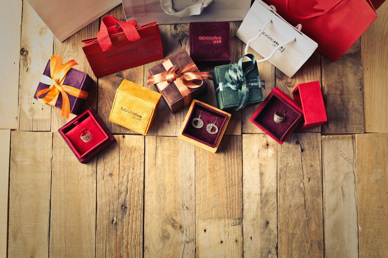 Colorful gift boxes and bags with ribbons on a wooden surface, containing elegant earrings and a ring.