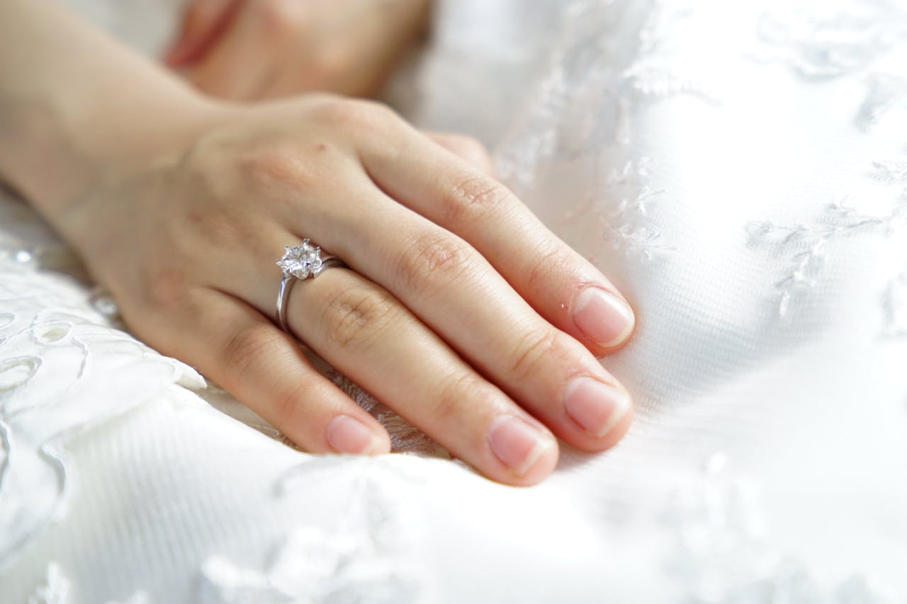 A close up of a bride&rsquo;s hand laying on top of the white fabric, showcasing white gold diamond engagement ring