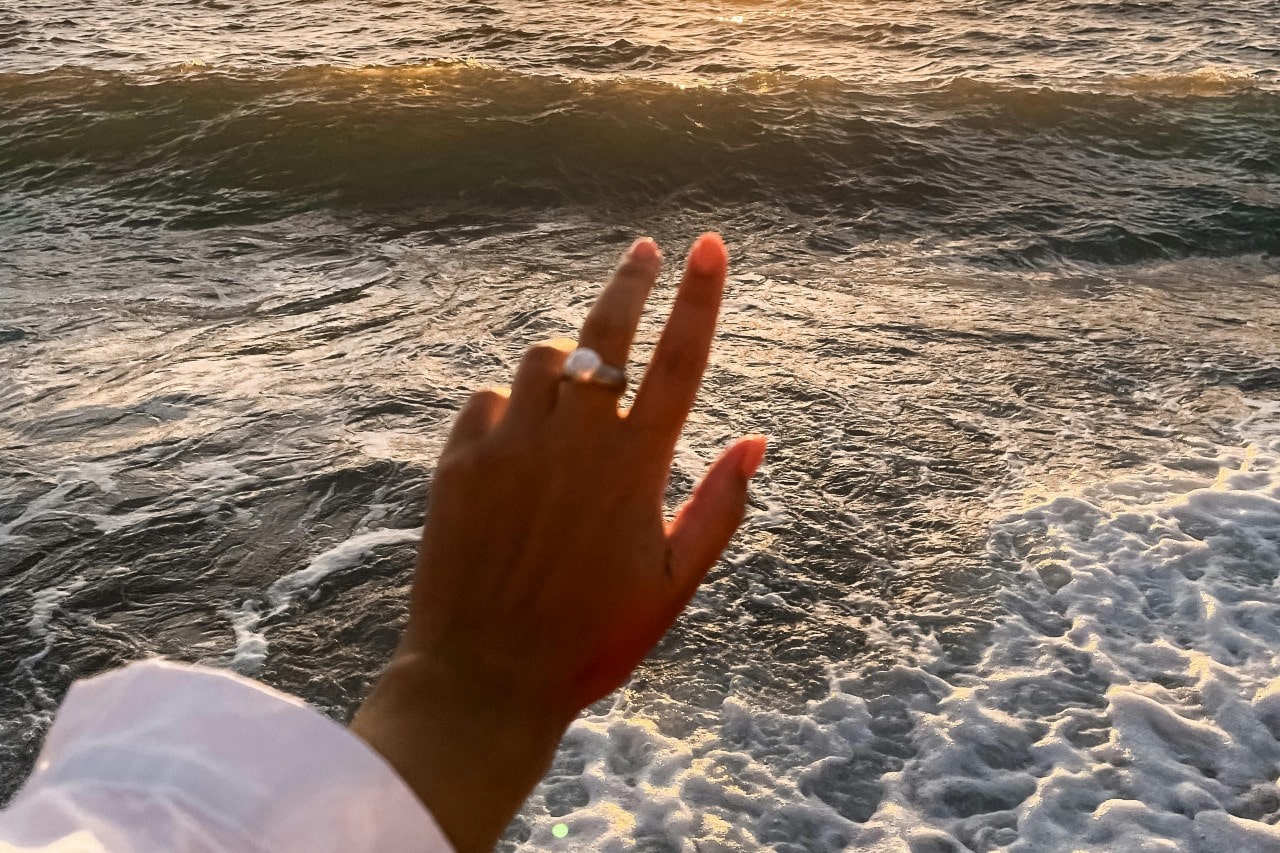 a woman’s hand extended toward the ocean wearing a bold cocktail ring