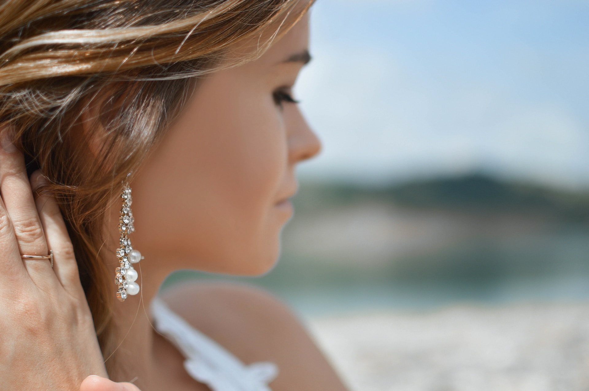 a woman on the beach wearing long dangly pearl and diamond earrings