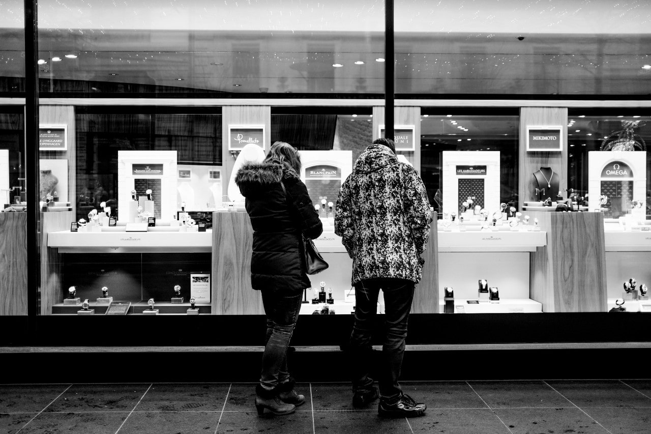 A black and white image of a young couple window shopping outside a luxury jewelry store.