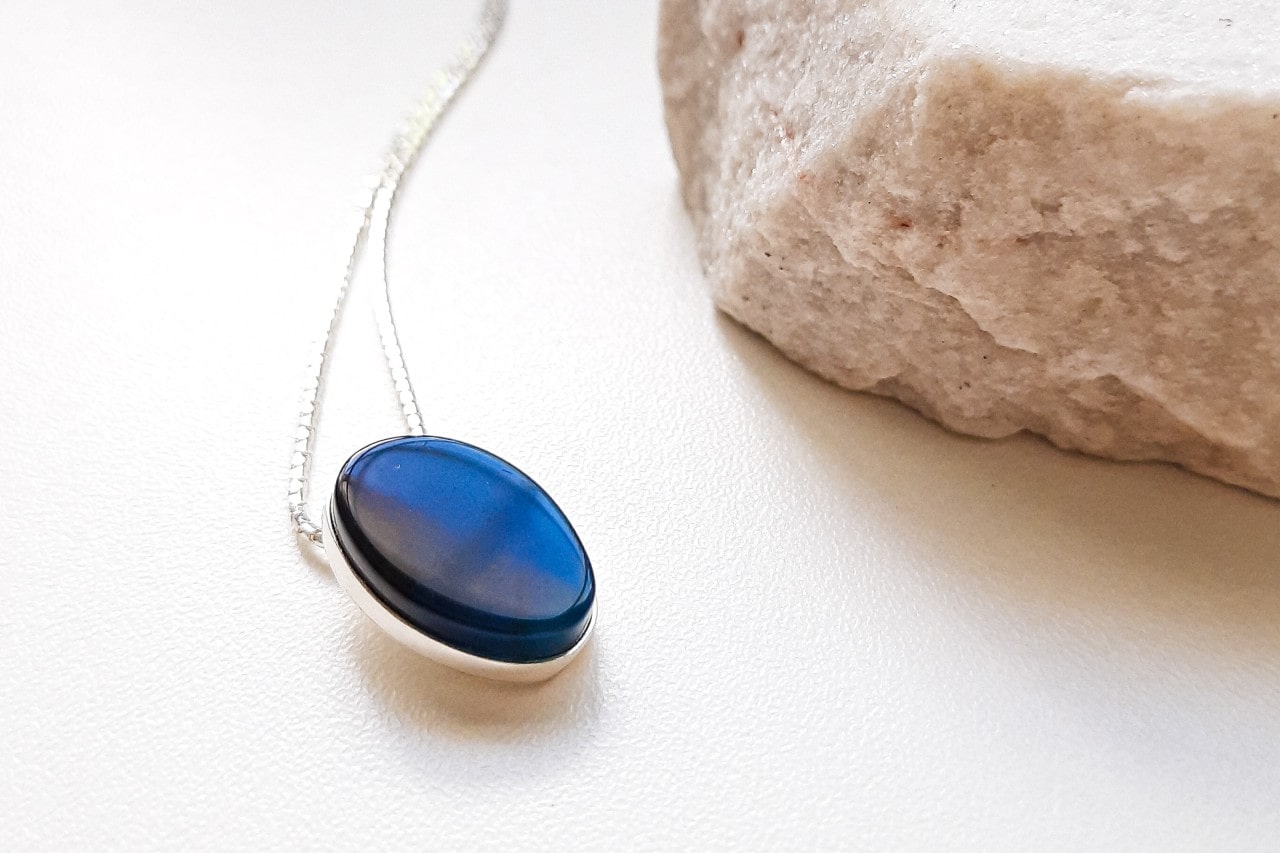 a white gold pendant necklace with a blue stone next to a white rock