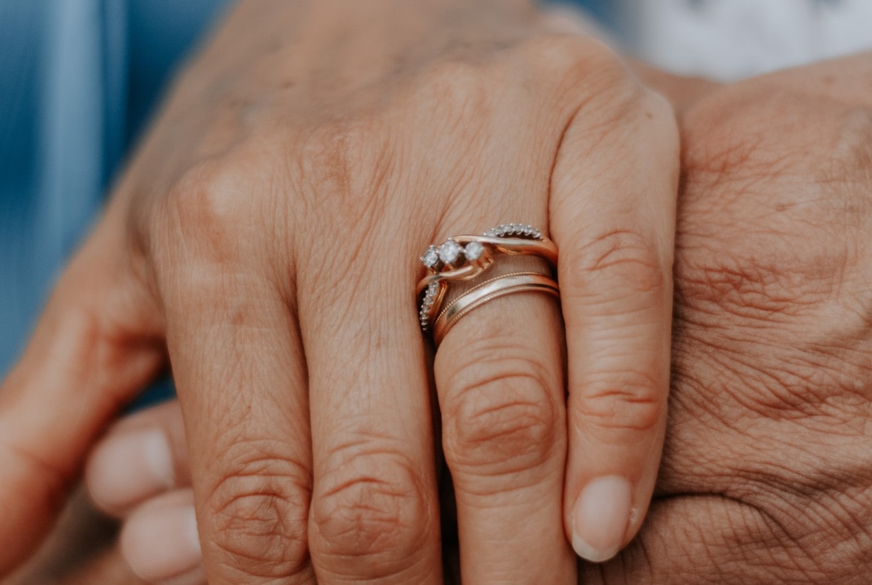 a woman’s hand wearing bridal rings clasped over a man’s hand