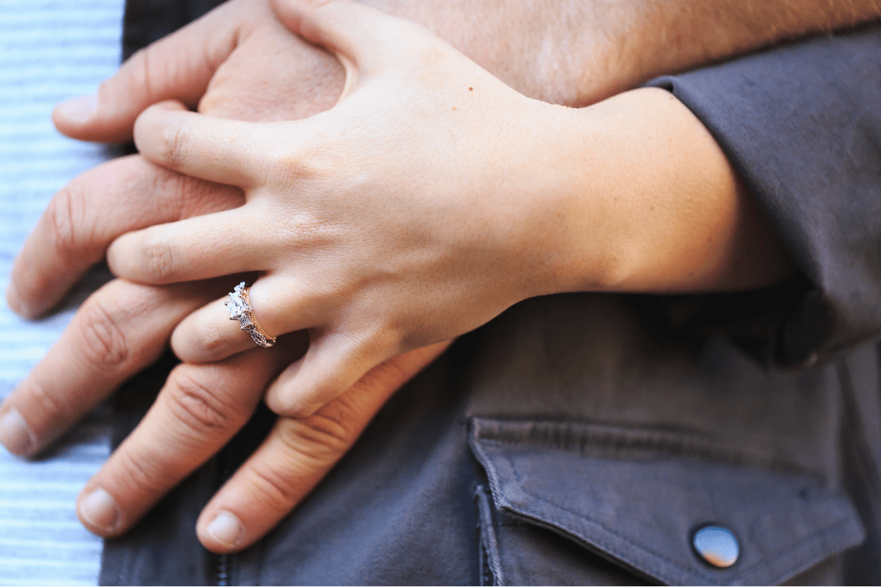 A woman intertwining her fingers on top of her partner's hand, showcasing her stunning engagement ring.
