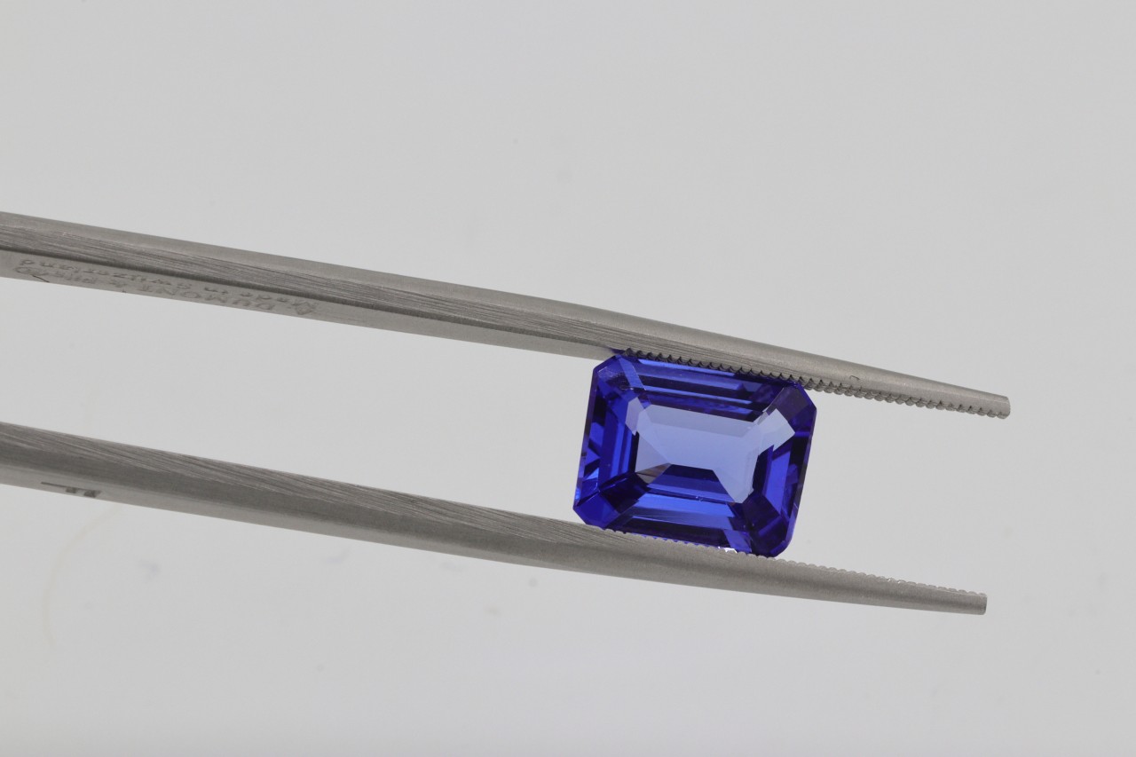 A pair of pliers holding an emerald shaped dark blue stone.