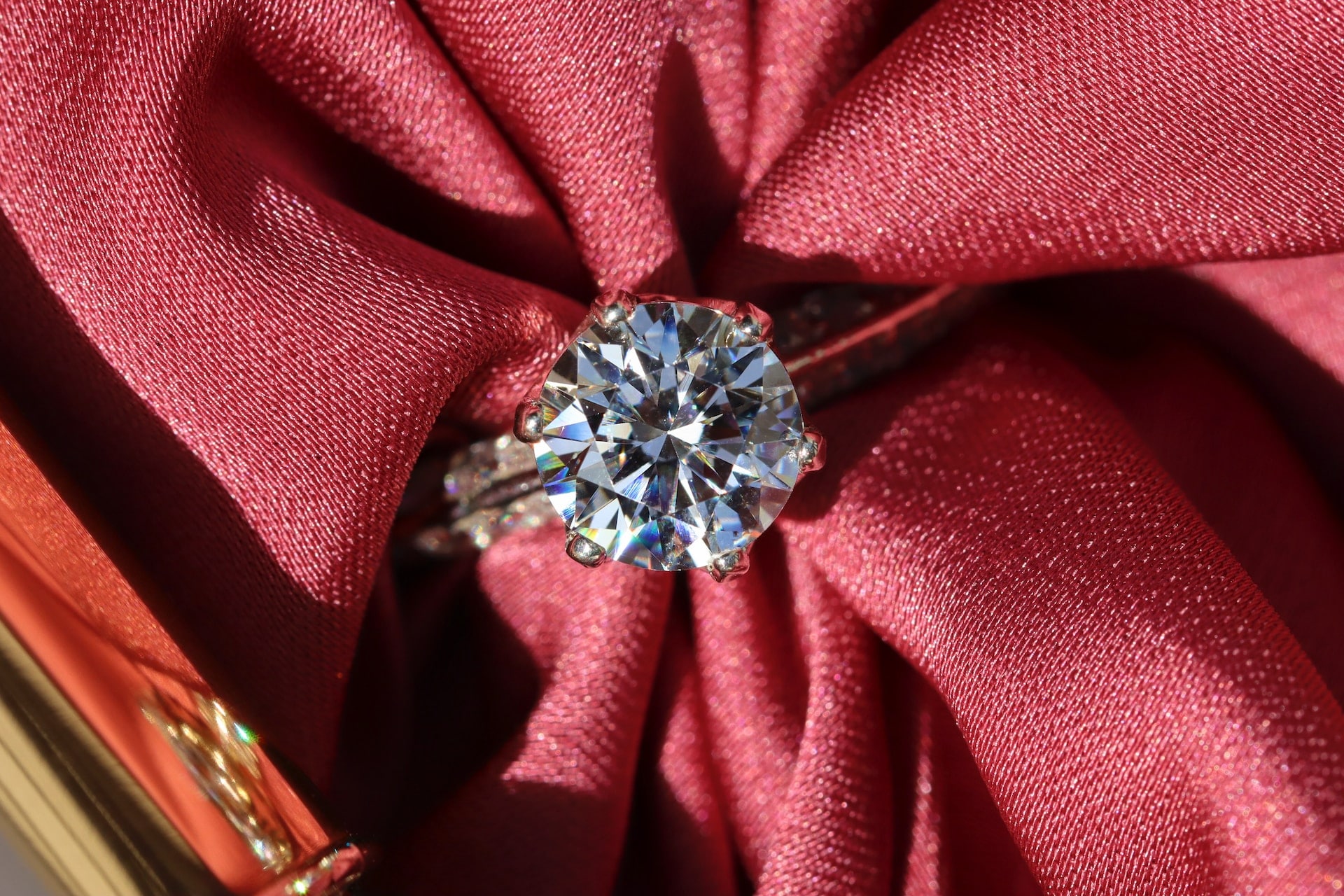 A gorgeous round diamond engagement ring with red fabric stuffed through it, a bright light shining down on it.