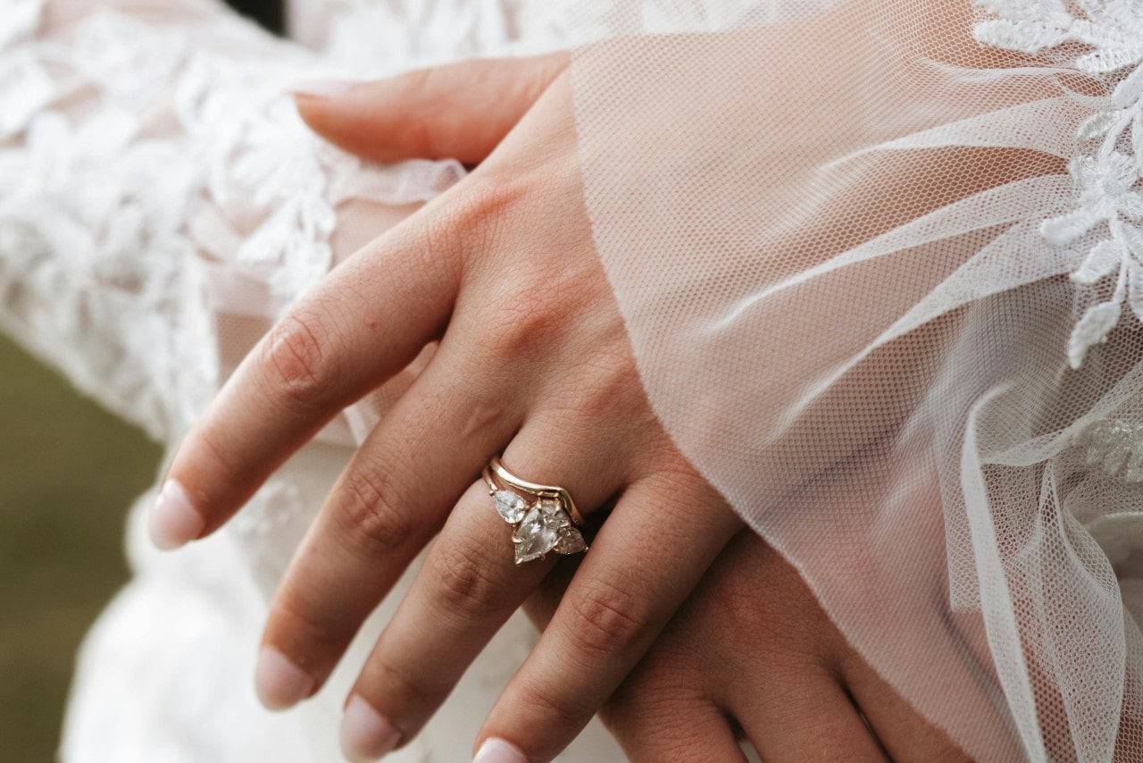A close-up of a bride-to-be’s hands, an elegant three stone engagement ring on her finger.