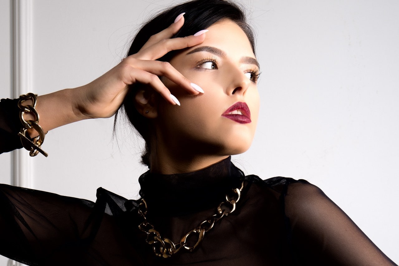 A model wearing a sheer black top showcases chunky chain necklaces from Armenta