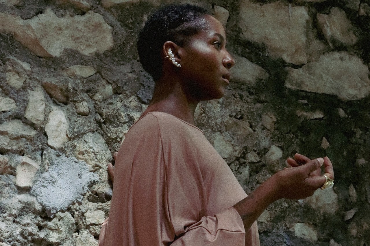 A woman wearing a dusty rose top and a pair of pearl crawler earrings.