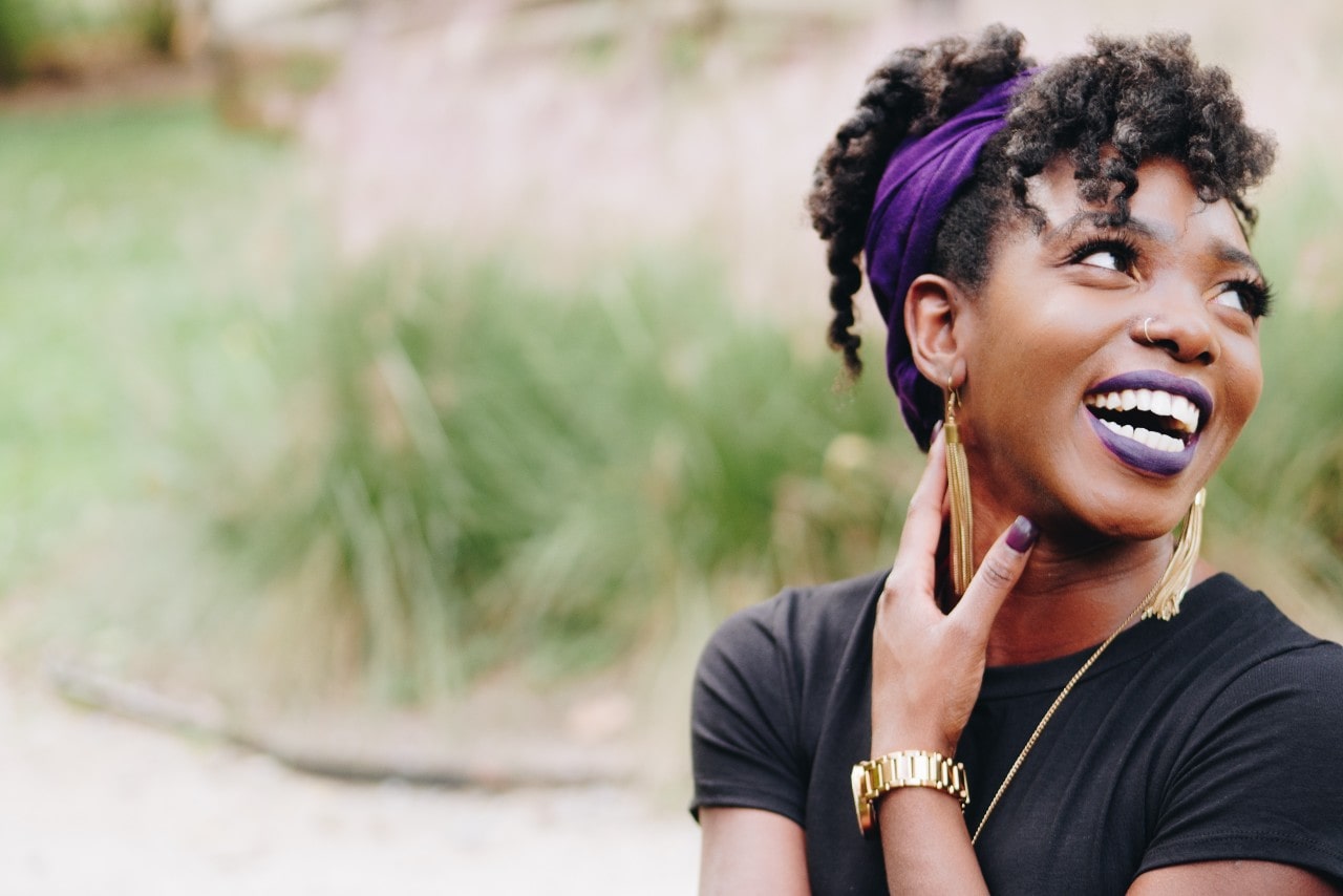 A woman walking through a park while wearing gold jewelry looks back and laughs.