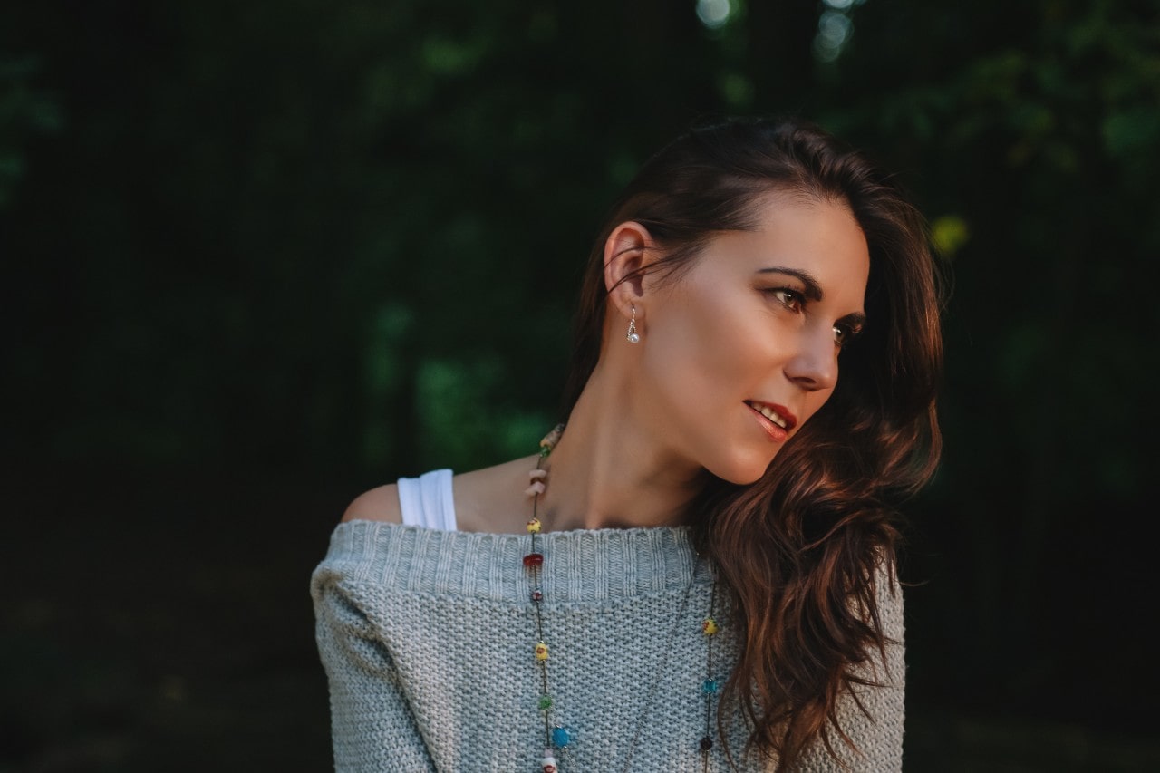 A woman wearing diamond earrings sits outside with her head tilted.