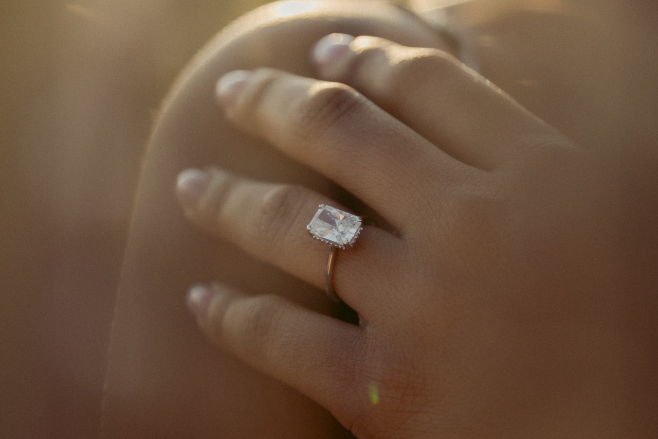 A close up of a woman’s hand resting on her shoulder, showcasing rose gold brilliant cut diamond engagement ring. A close up of a woman’s hand resting on her shoulder, showcasing rose gold brilliant cut diamond engagement ring.