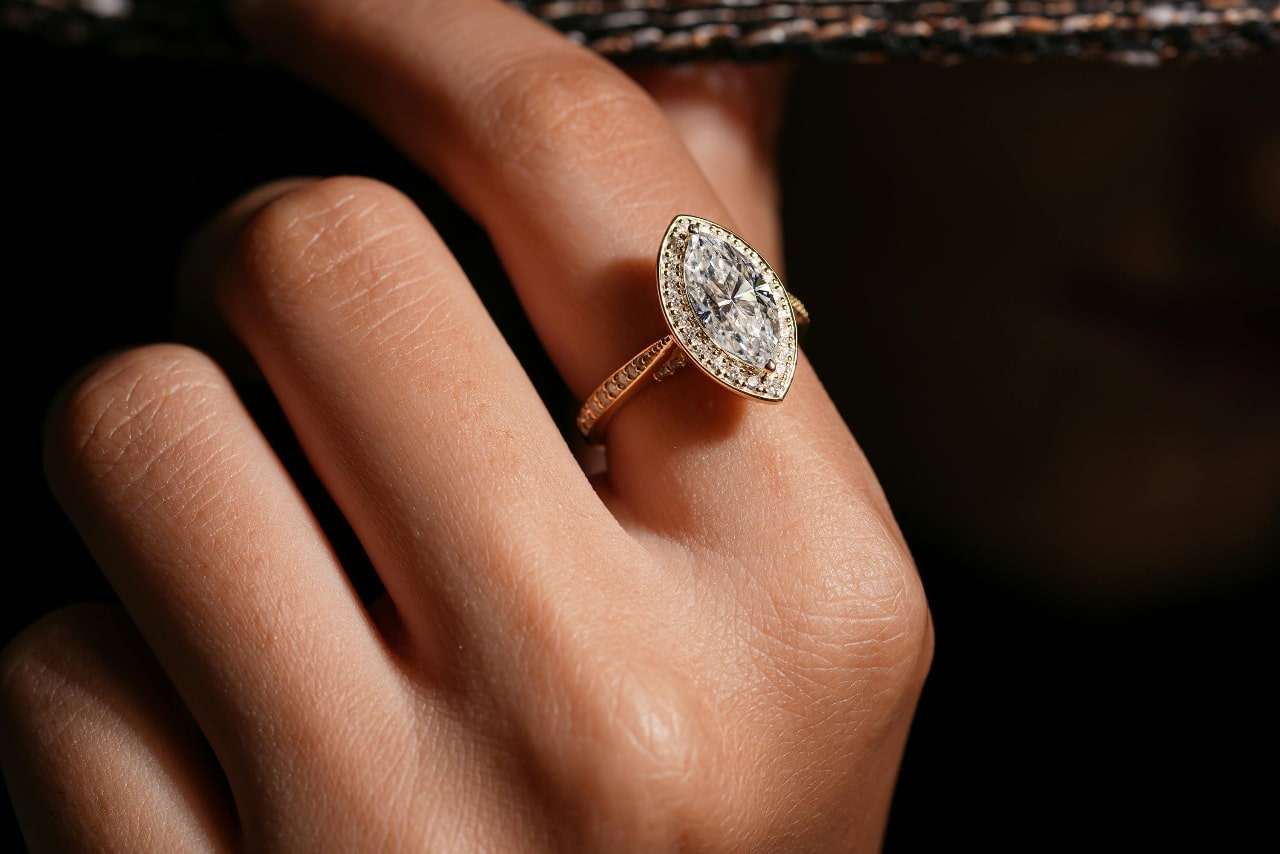 A close up of an ornate marquise engagement ring on a woman’s finger. A close up of an ornate marquise engagement ring on a woman’s finger.