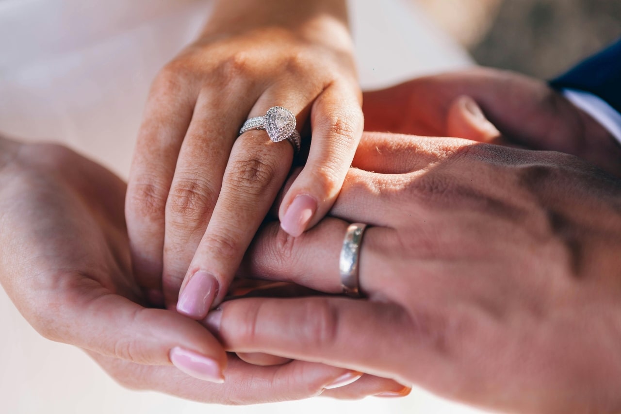A close-up of a couple holding hands, with emphasis on the bride’s ornate pear cut halo ring.
