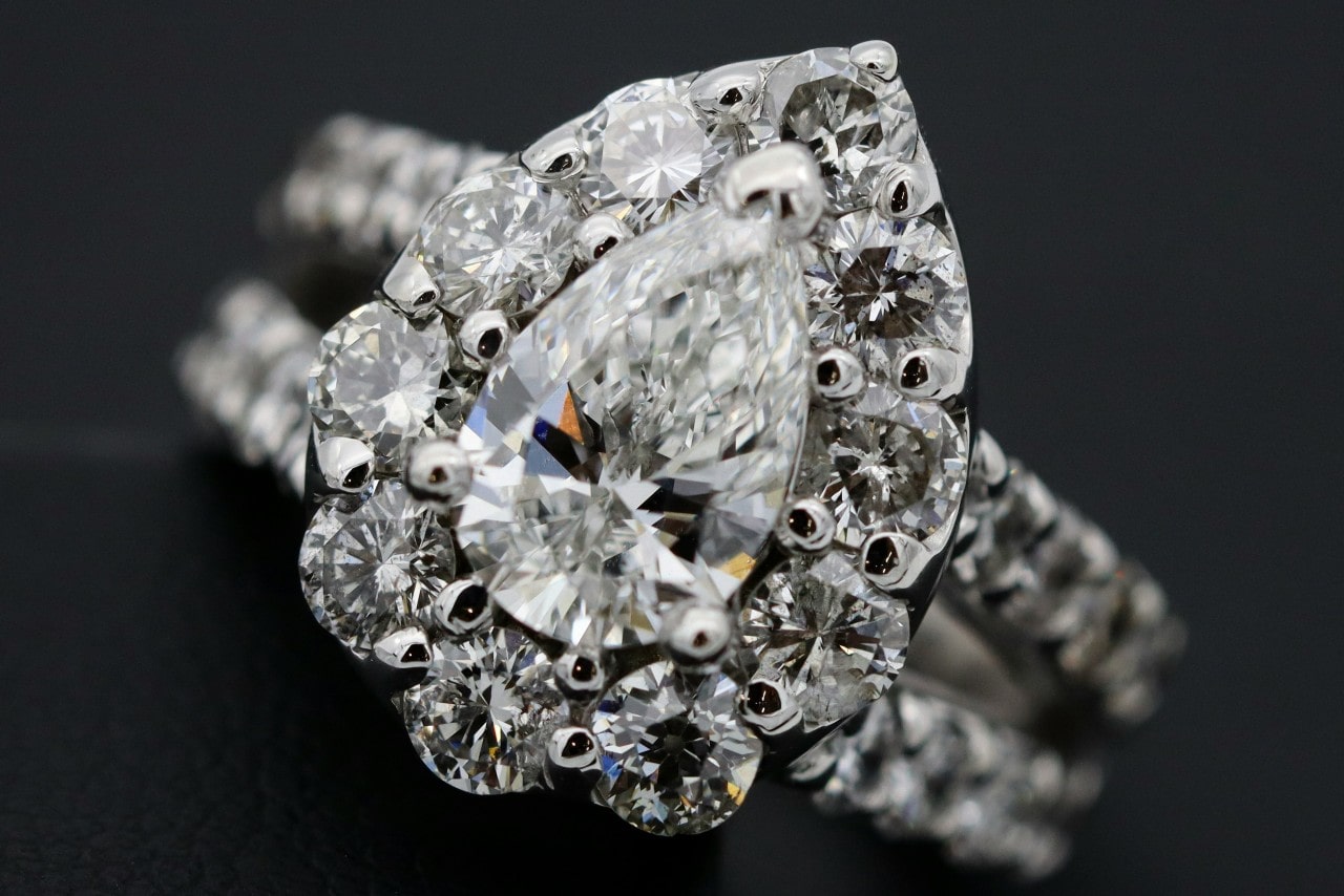 A close-up of an opulent halo ring with a pear cut center stone and a split shank band covered in accent diamonds.