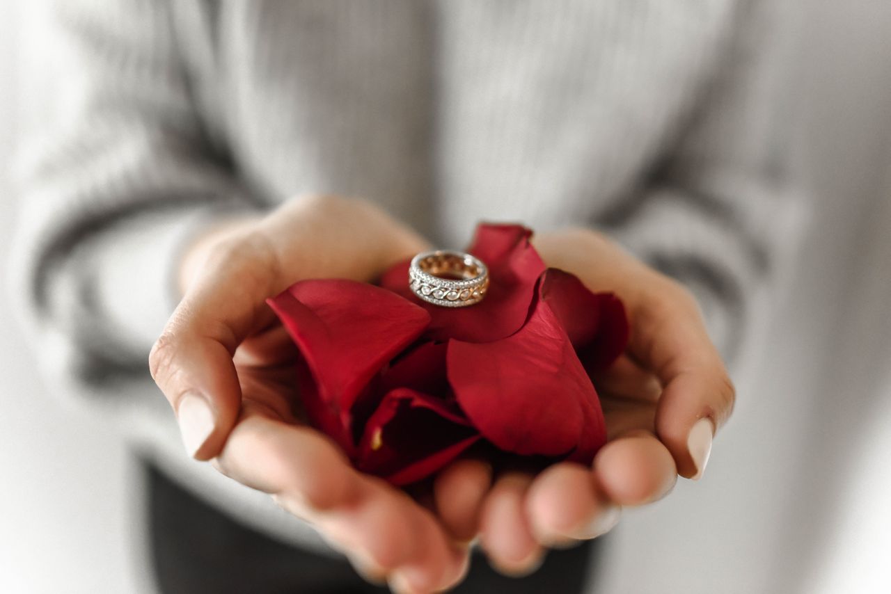 A detailed diamond ladies’ wedding band held in outstretched hands resting on rose petals