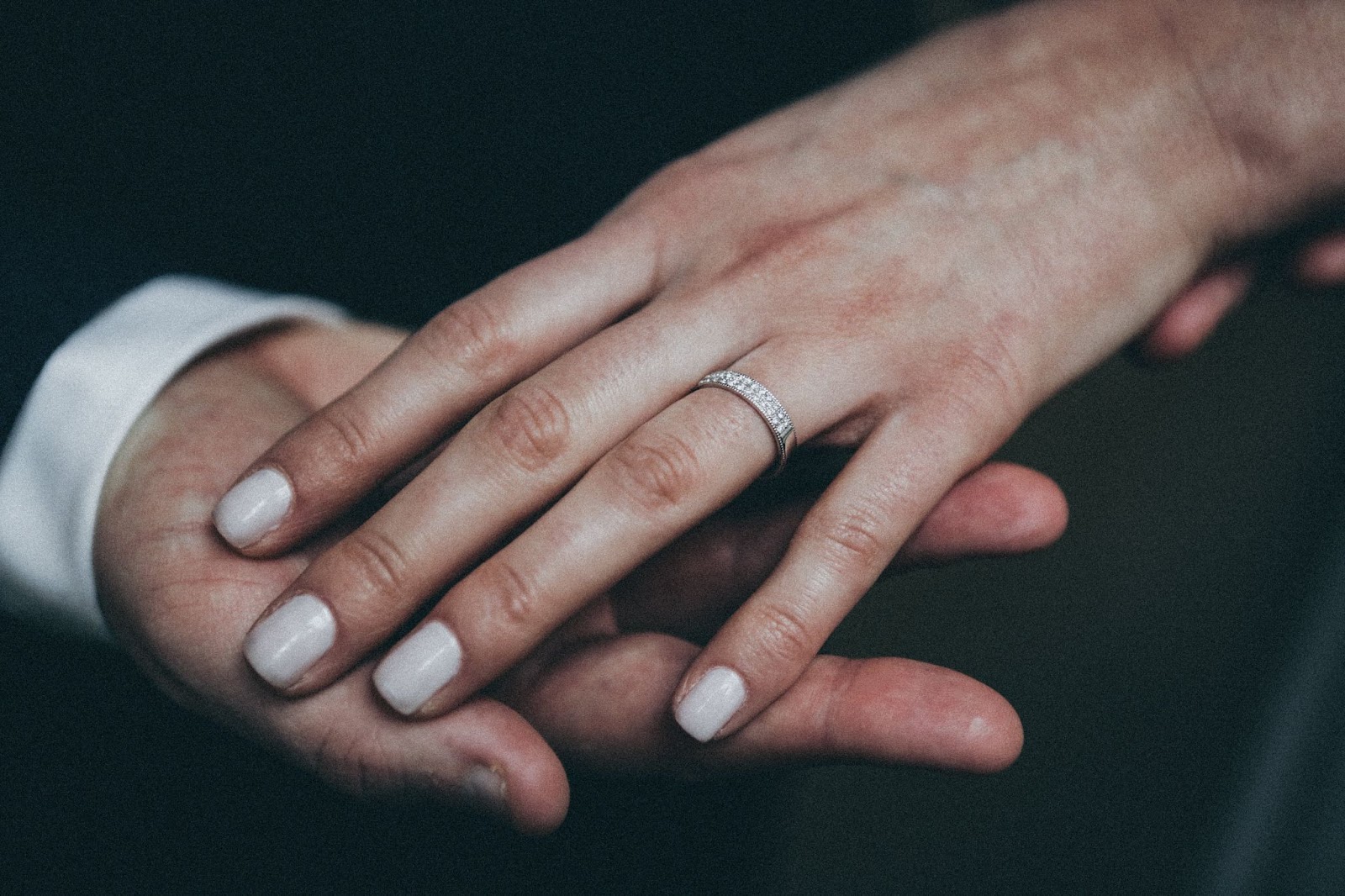 A woman’s hand being held by her groom’s and wearing a diamond wedding band