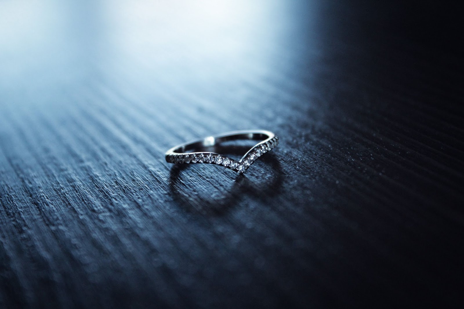 A silver ladies’ wedding band with curved silhouette and diamonds against dark background