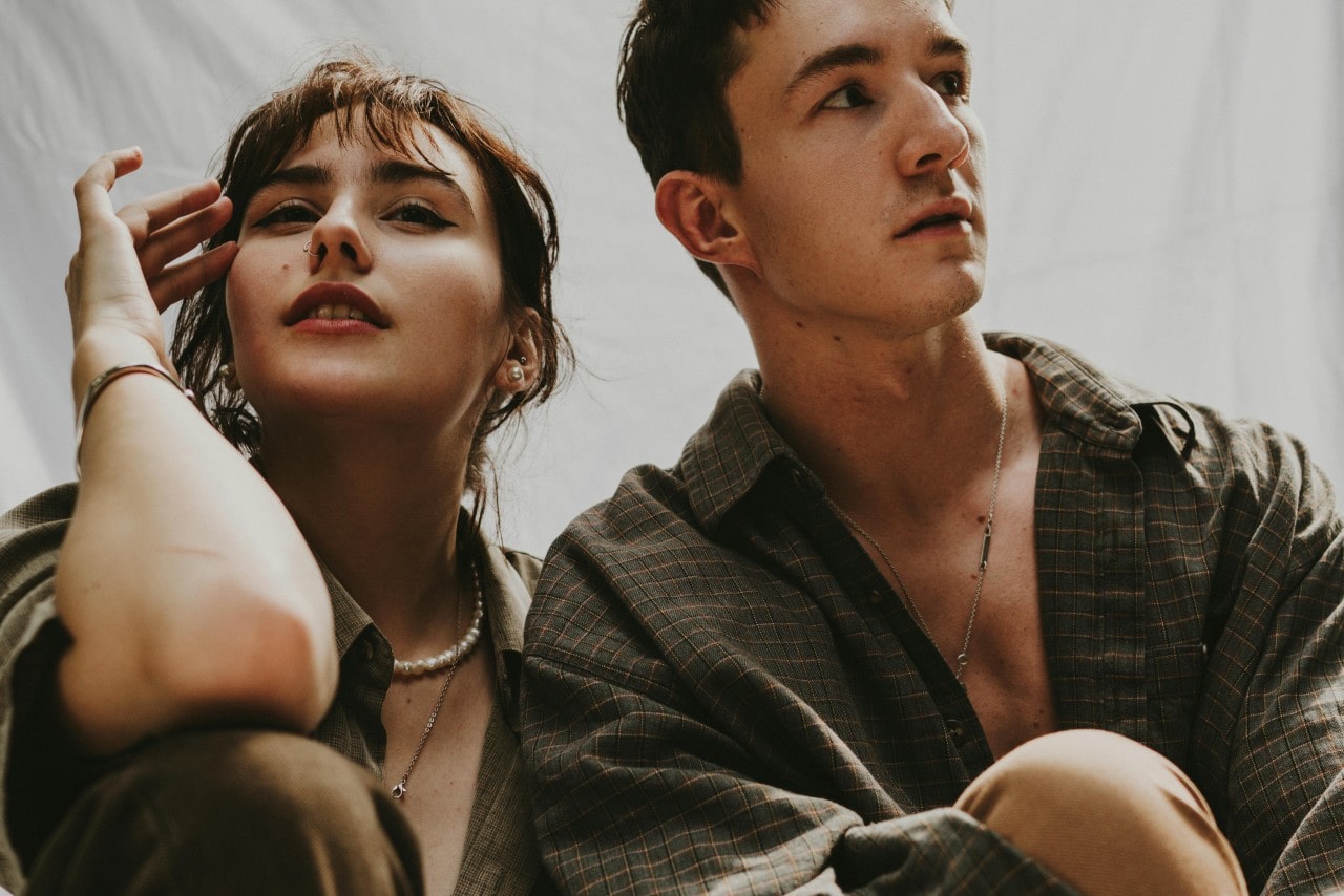 A young couple in plaid sits close, their sparkling jewelry stealing the spotlight against a neutral backdrop.