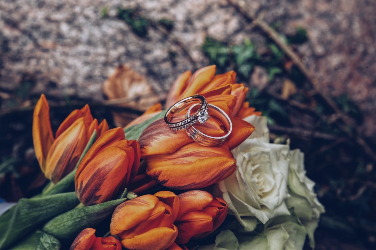 Round cut diamond ring with diamonds going around the band sitting on top of a bouquet of tiger lilies