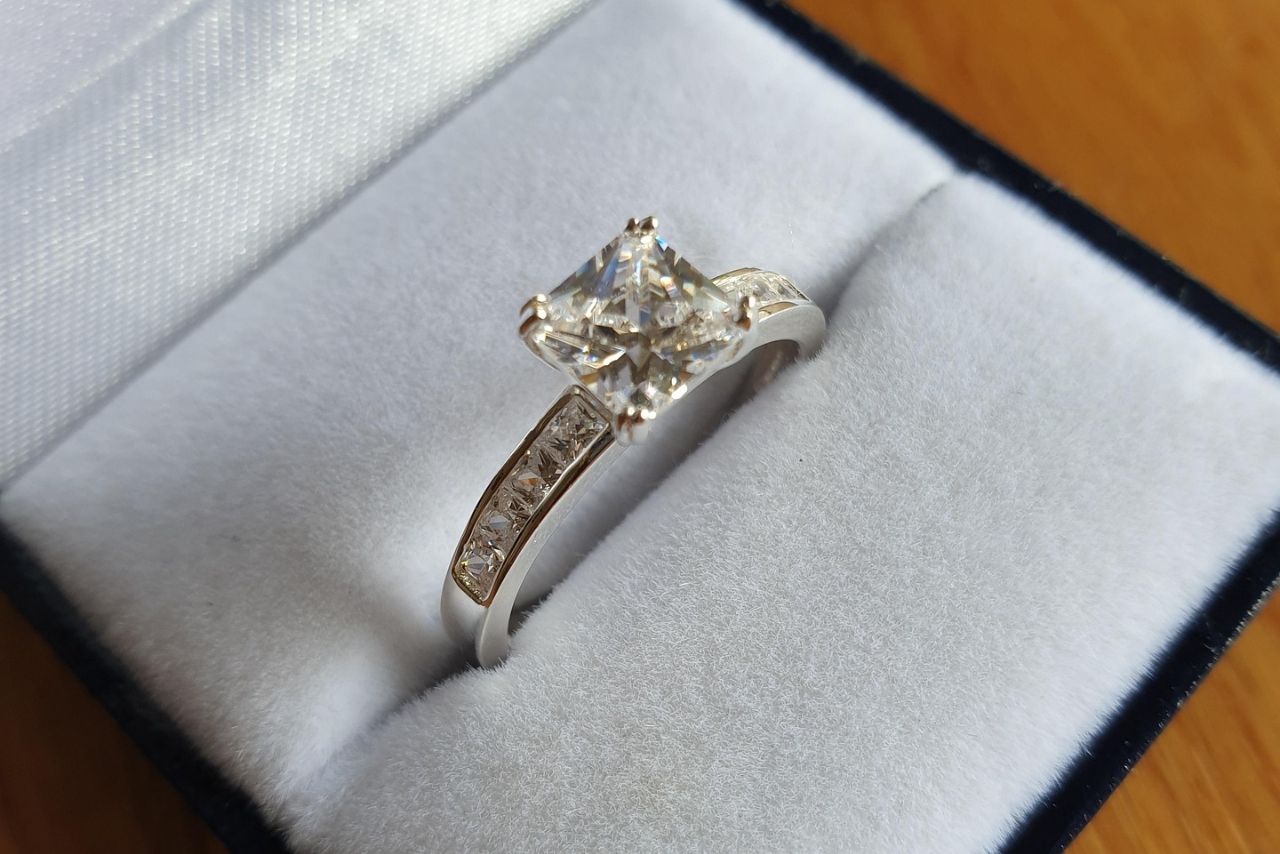 A close-up of a princess-cut side-stone diamond engagement ring in a gray ring box.