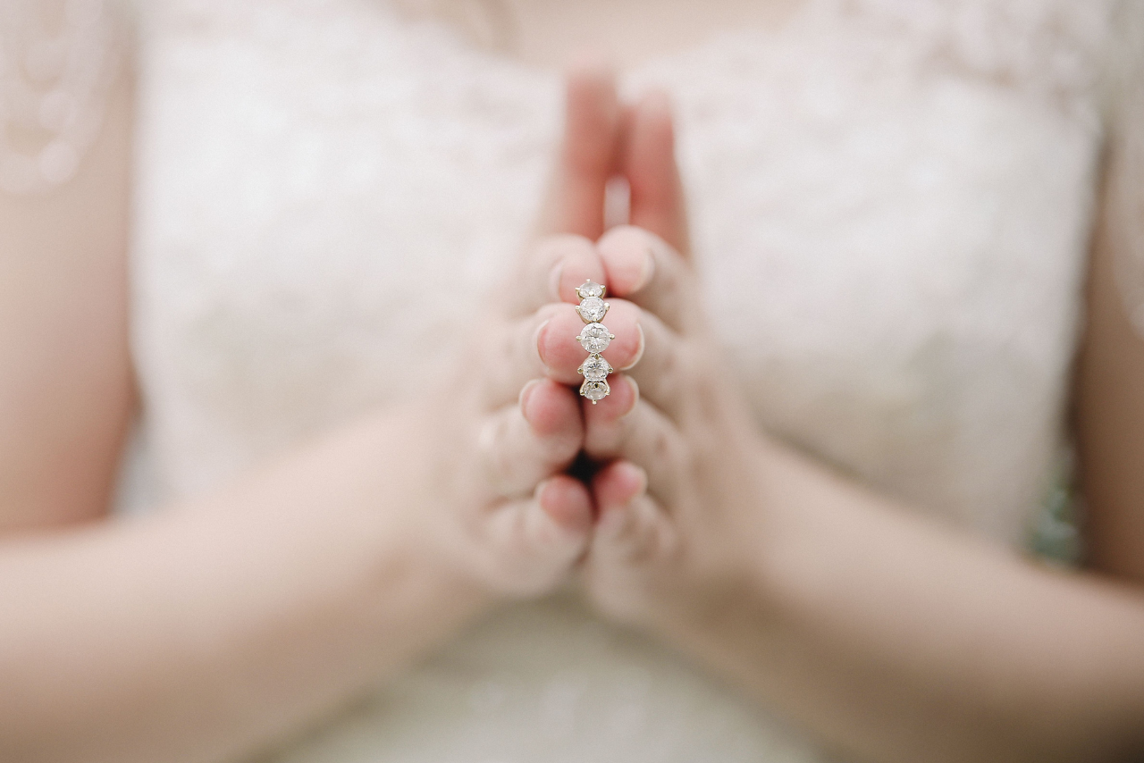 A woman in her wedding dress holding a diamond engagement ring in between her hands.