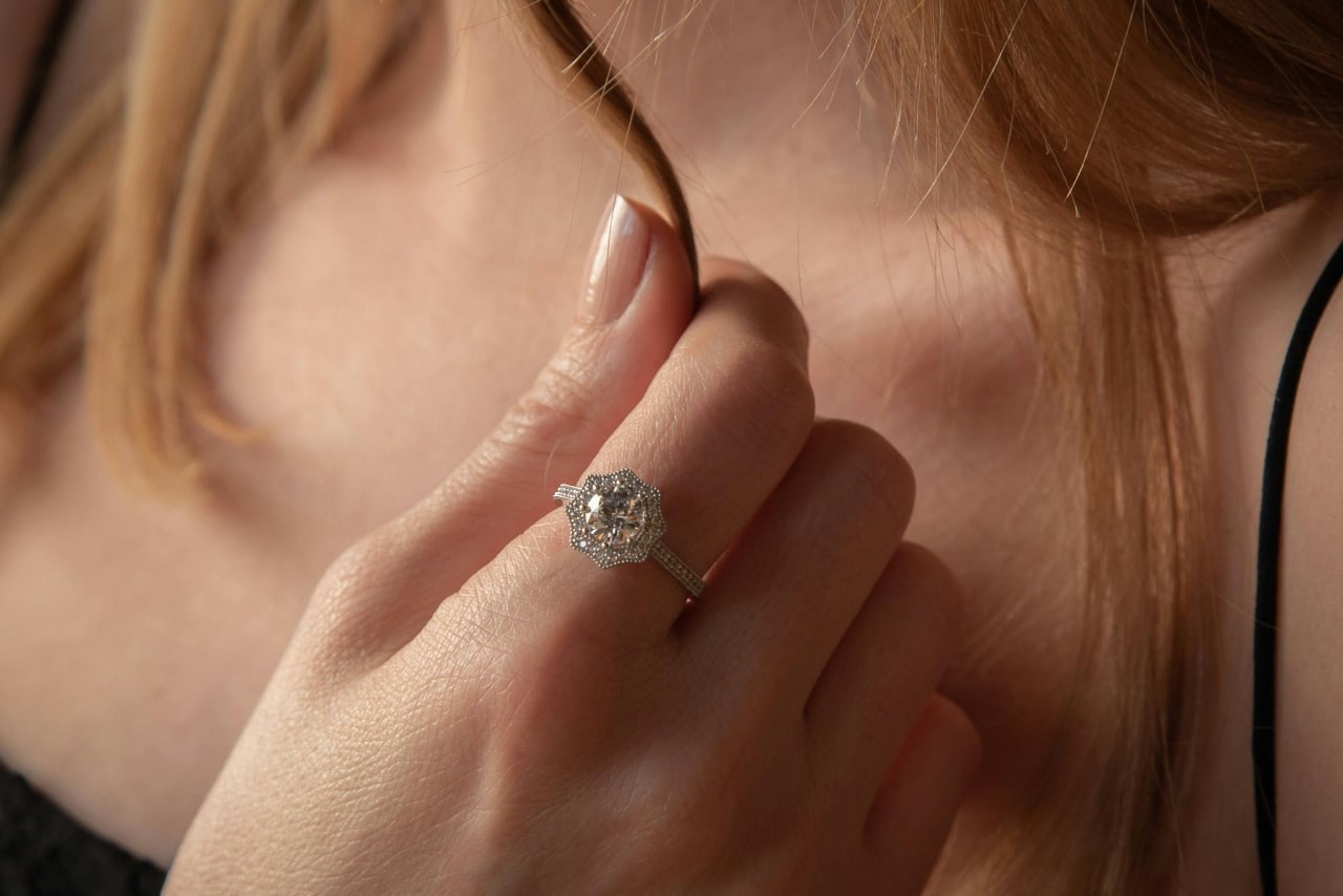 A woman with red hair holding on to a strand of it, showcasing her halo engagement ring.