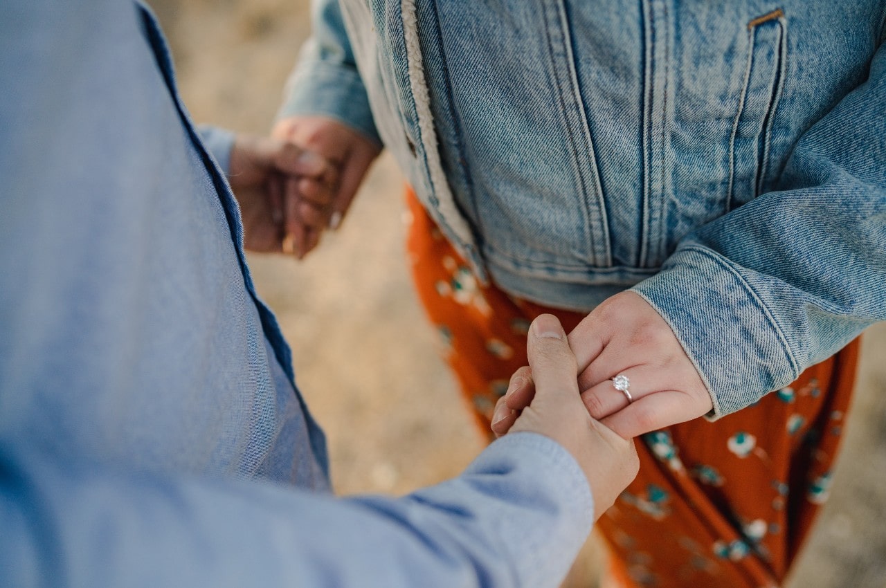 A dressed-up couple holds hands and shows off a Sylvie solitaire engagement ring