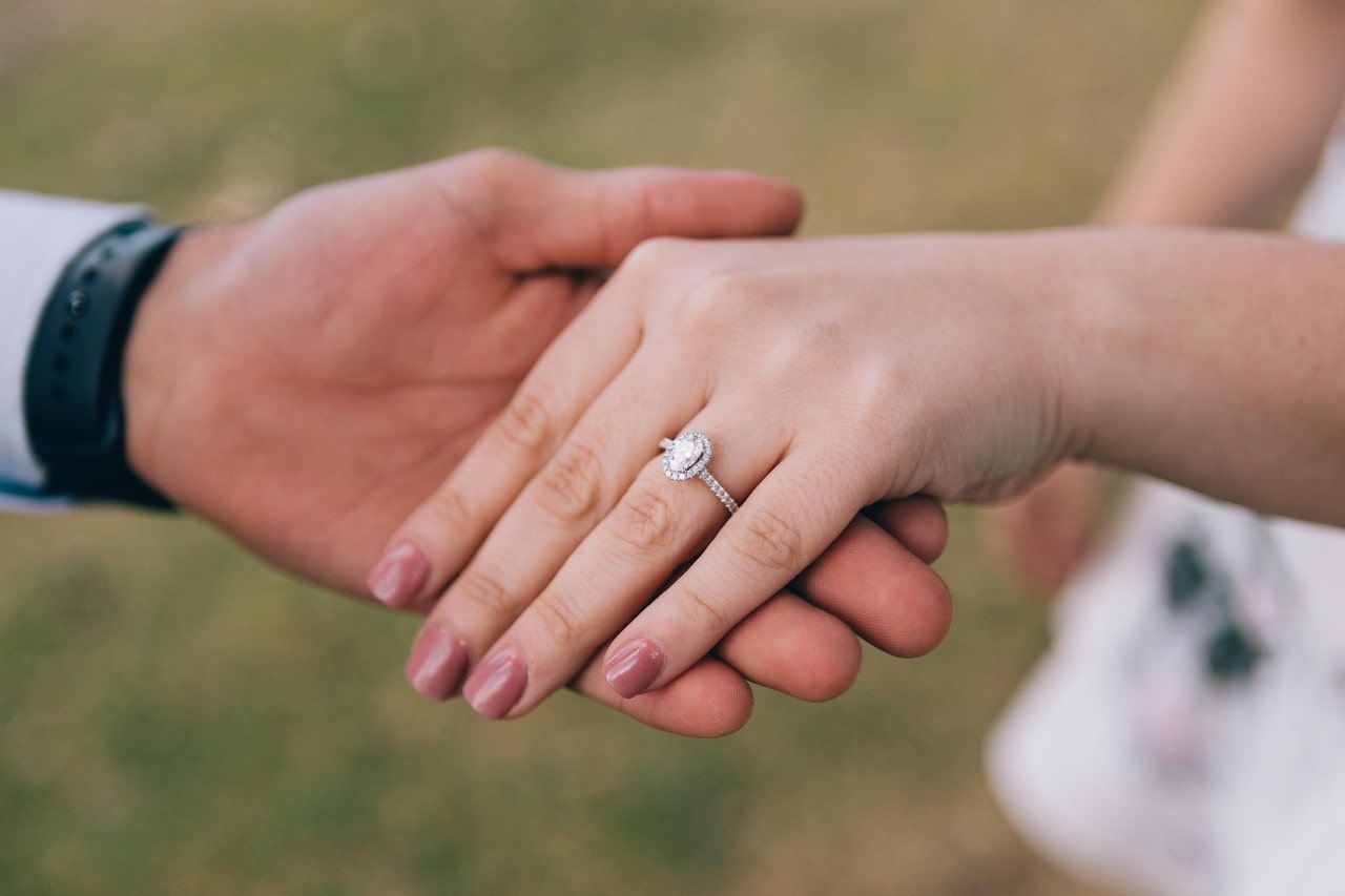 A man inspects his bride’s oval-cut diamond halo engagement ring while on a walk