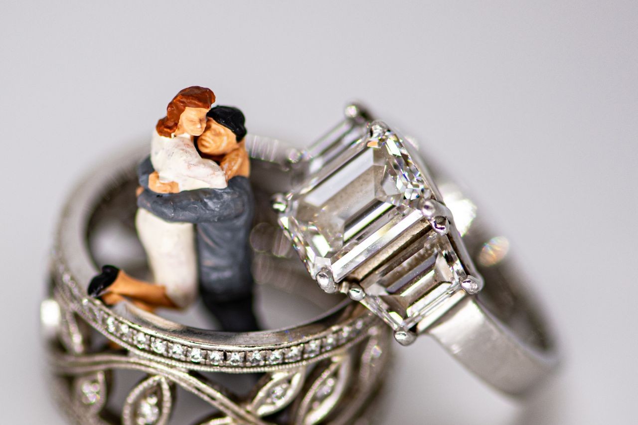 Two white gold rings and a bride and groom cake topper. The engagement ring features three diamonds