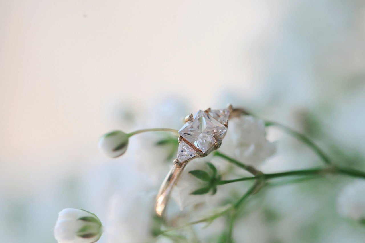 Gold three stone engagement ring hanging on a flower’s stem