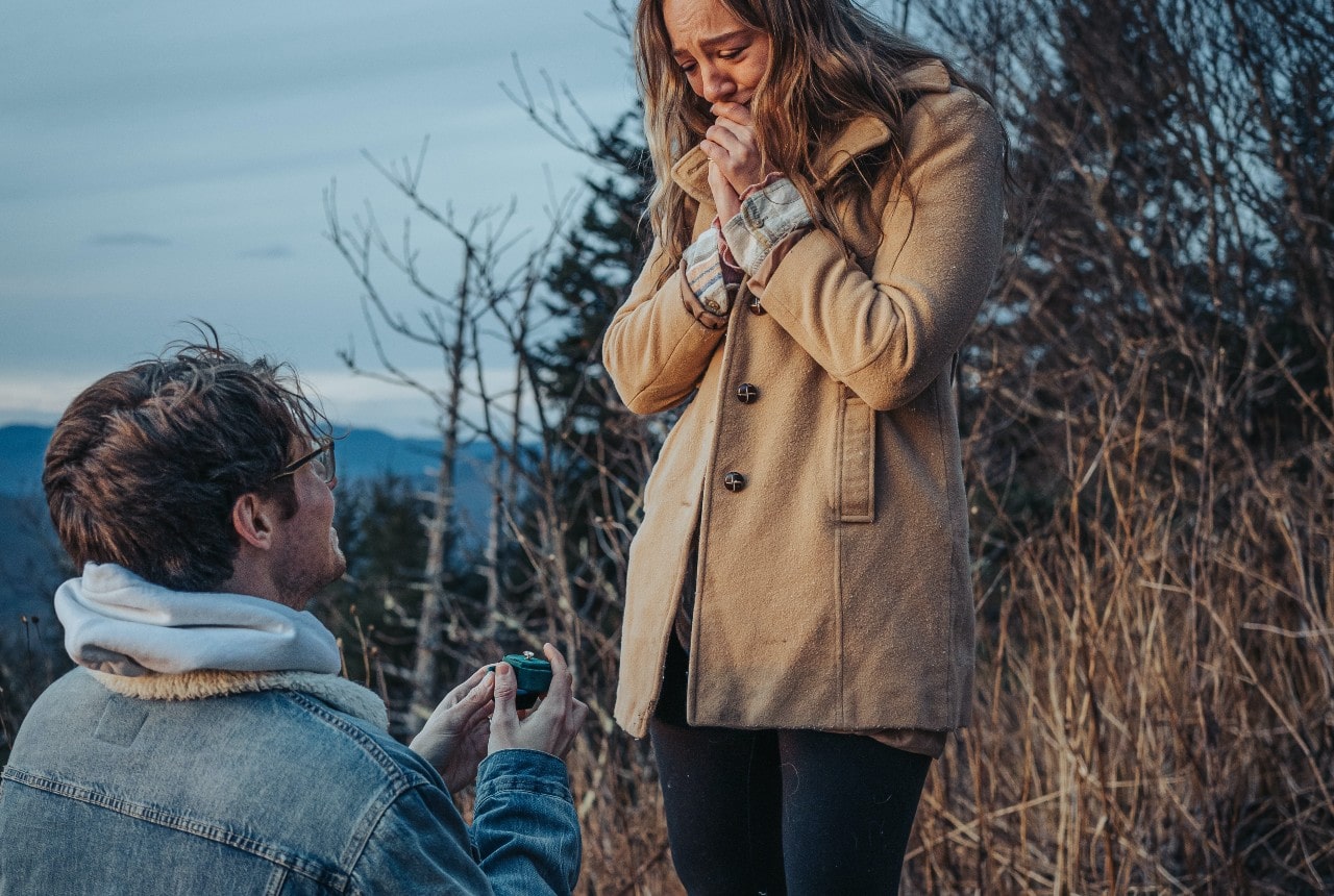 Man down on one knee, presenting a ring to his future bride outdoors