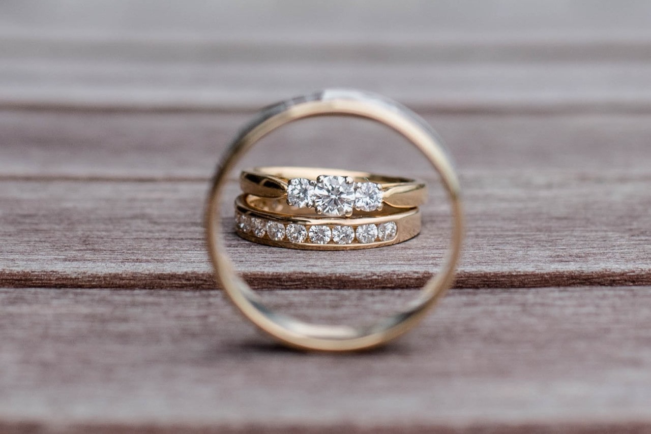 A gold band frames a wedding ring and wedding band on a wooden surface.