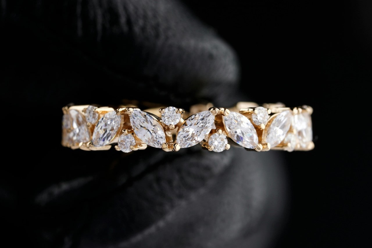 An elegant gold band with alternating marquise and round-cut white stones held by a gloved hand.