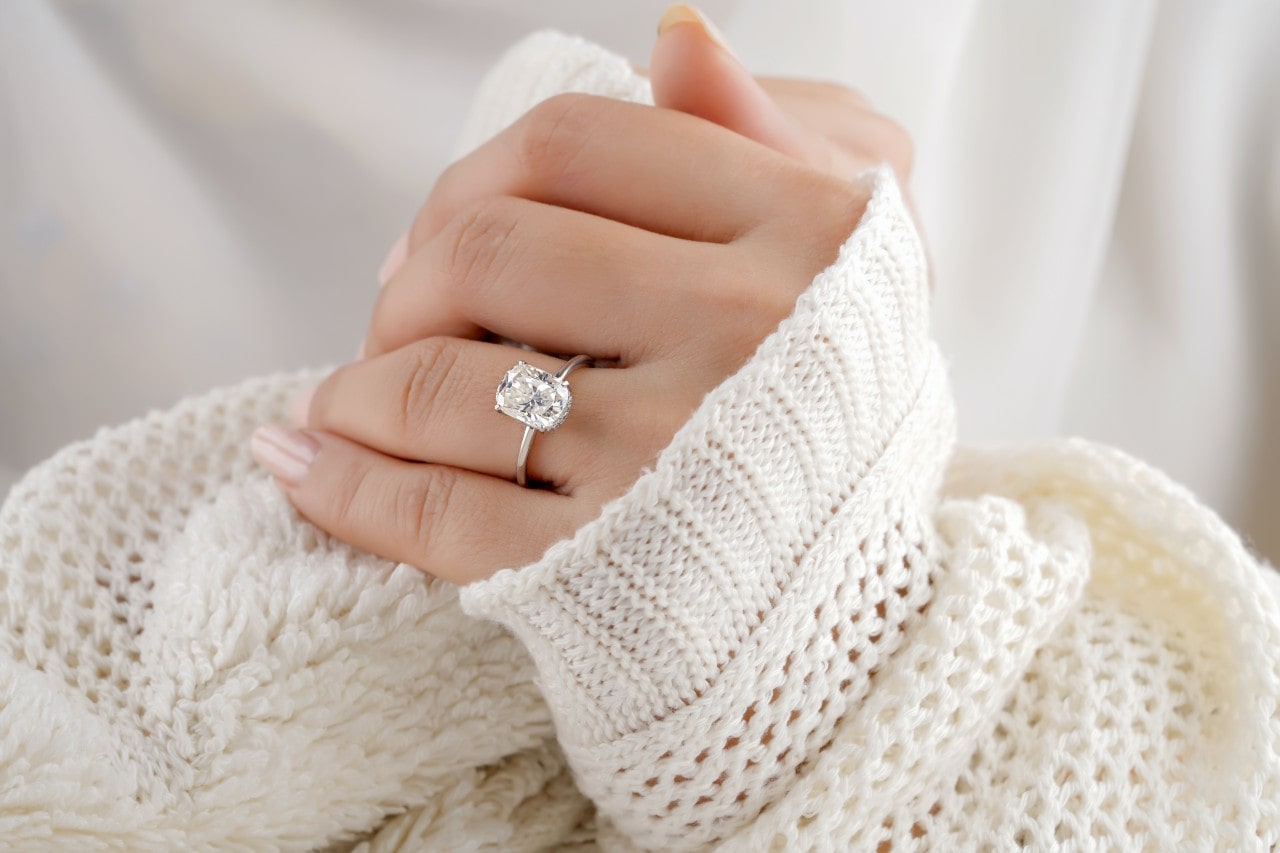 close up image of a woman wearing a sweater and a white gold solitaire engagement ring