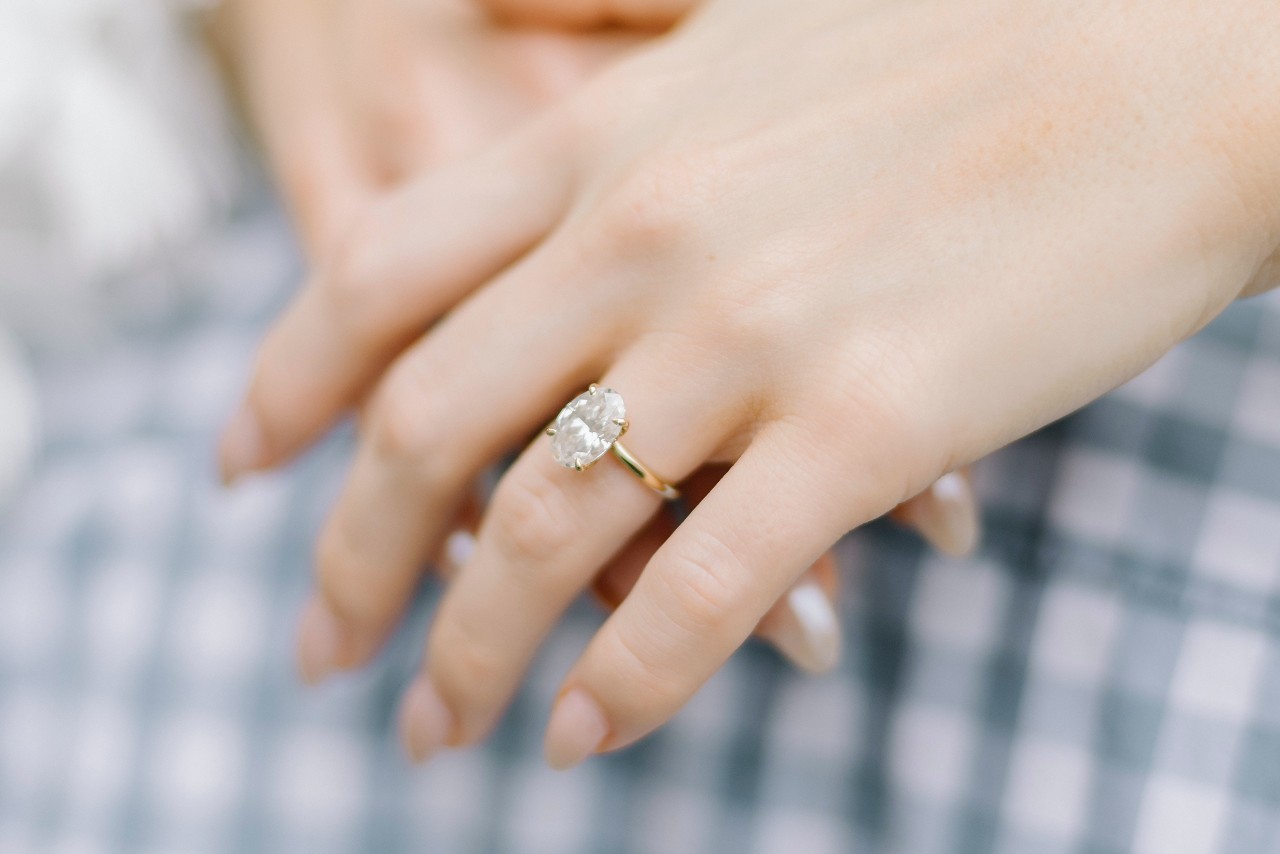 close up image of a woman’s hands crossed over each other, wearing a yellow gold solitaire engagement ring