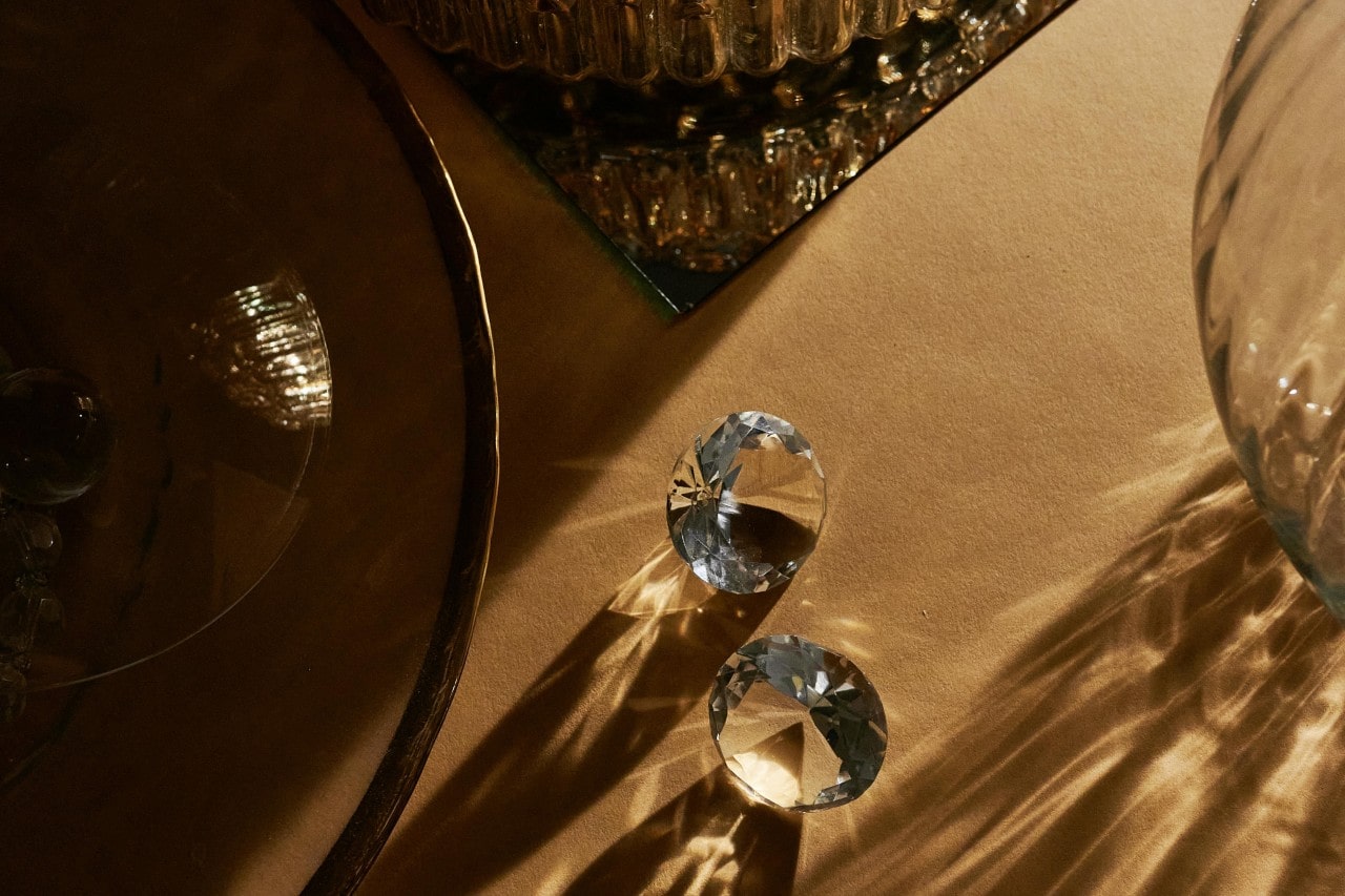 two round cut diamonds sitting on a beige table next to pieces of glassware two round cut diamonds sitting on a beige table next to pieces of glassware