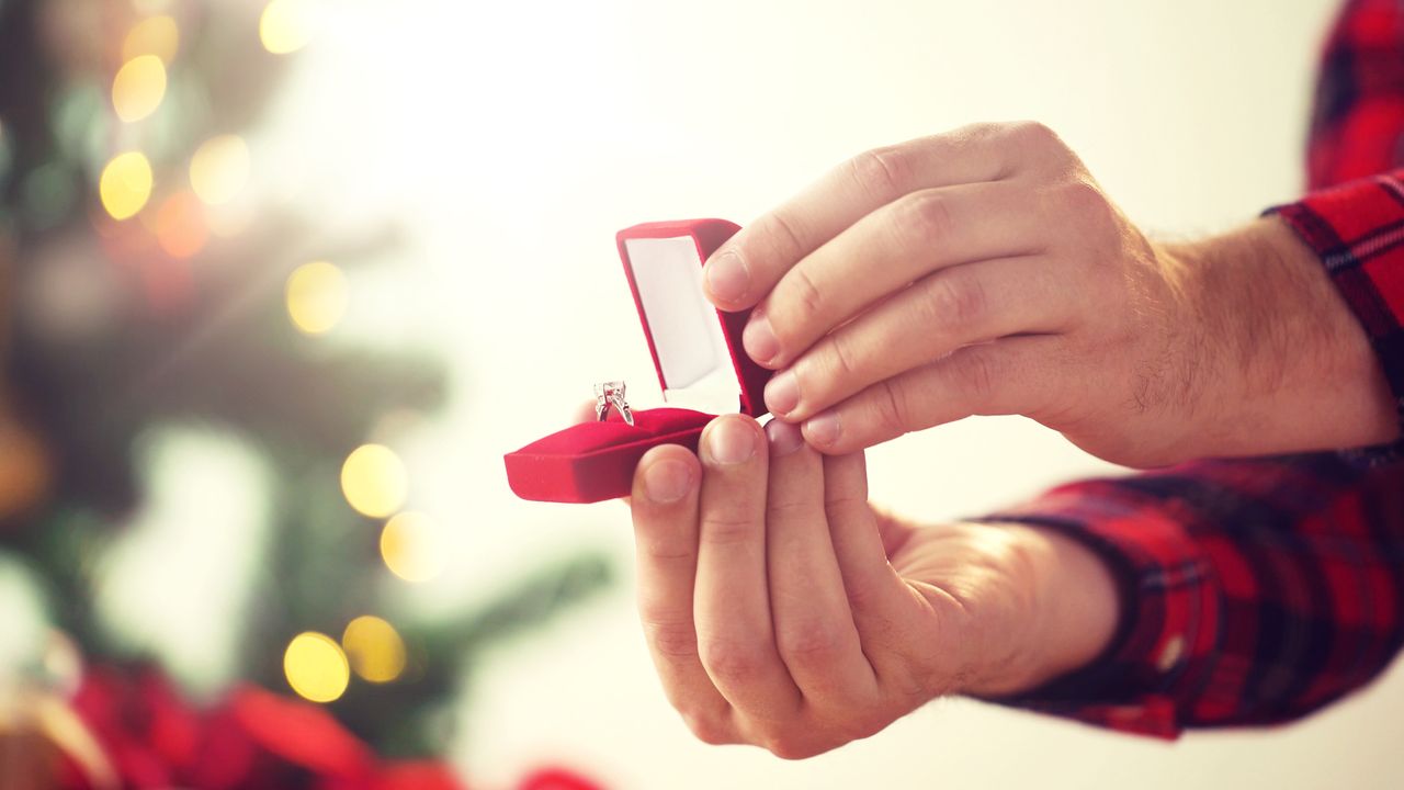 a man holding a jewelry box presenting a simple engagement ring