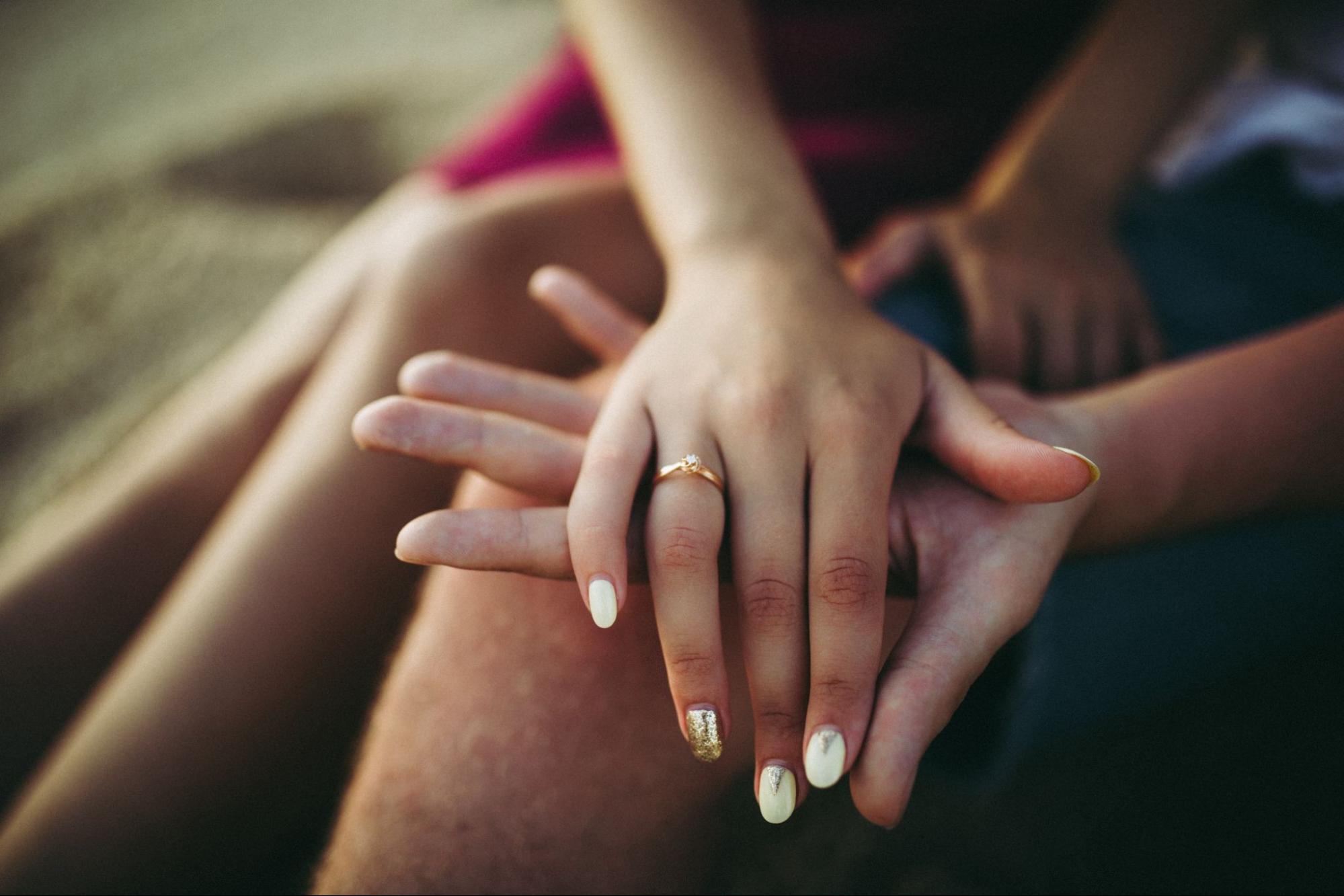 a lady’s hand wearing a simple engagement ring clasped over a man’s hand